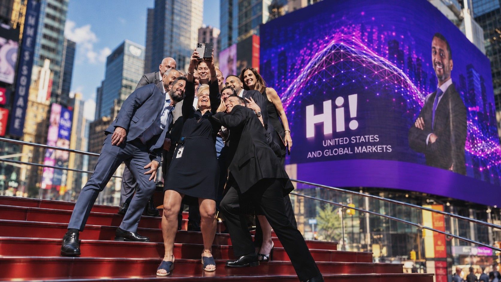 Une équipe en selfie sur les marches rouges de Times Square, devant un écran géant